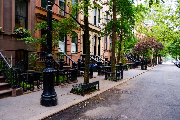 Rij bruinstenen huizen met stoepjes en smeedijzeren hekken langs een straat vol bomen in New York