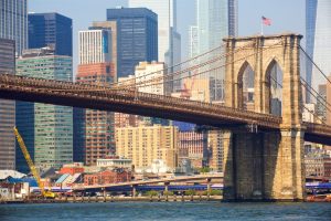 De stenen pijlers en kabels van de Brooklyn Bridge met wolkenkrabbers van Lower Manhattan en een gele bouwkraan op de achtergrond