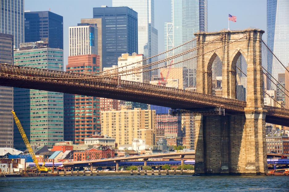 De stenen pijlers en kabels van de Brooklyn Bridge met wolkenkrabbers van Lower Manhattan en een gele bouwkraan op de achtergrond