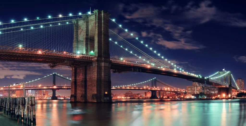De verlichte Brooklyn Bridge en Manhattan Bridge steken 's nachts boven de East River uit in New York