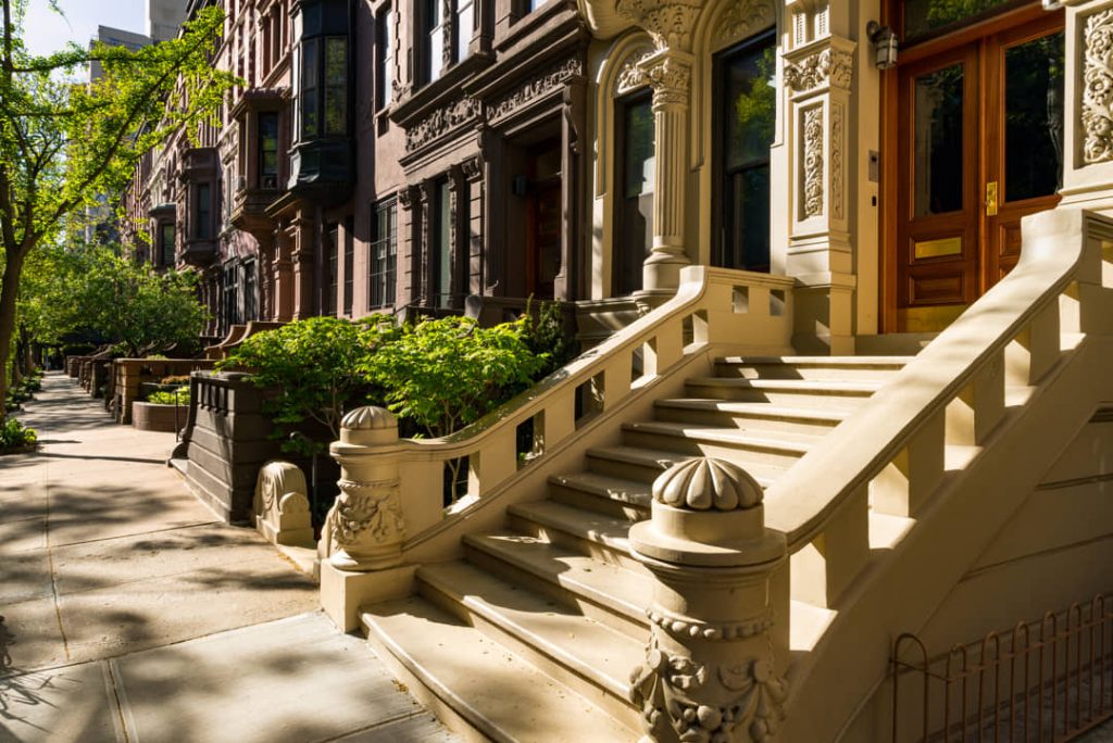 Zonnige straat met een rij statige bruinstenen herenhuizen, stoepjes en groene bomen in New York