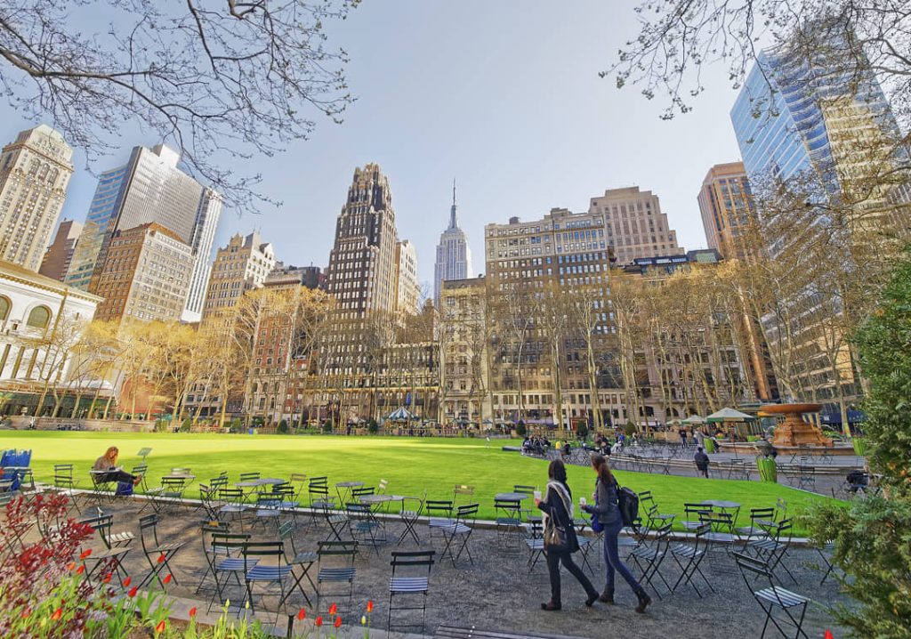 Groen gazon van Bryant Park met stoelen en tafeltjes en het Empire State Building zichtbaar tussen de gebouwen op de achtergrond