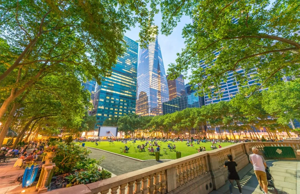 Grasveld in Bryant Park met filmscherm en bezoekers terwijl de torenspits van One World Trade Center zichtbaar is tussen bomen