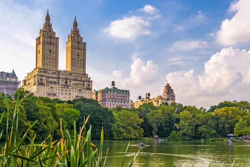 Groen meer in Central Park met een roeiboot terwijl de twee torens van het San Remo gebouw oprijzen