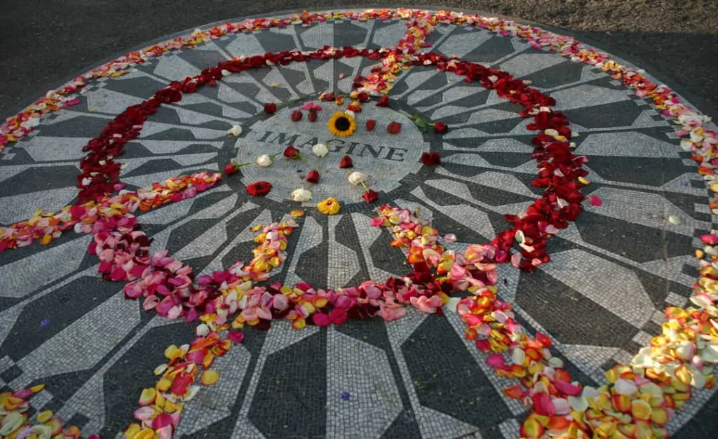Rond mozaïek met het woord Imagine op de grond in Strawberry Fields in Central Park New York, bedekt met kleurrijke bloemblaadjes en een zonnebloem