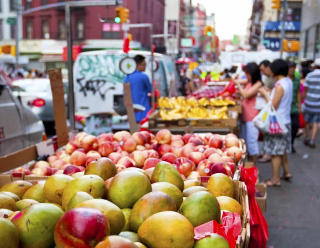 Kratten met verse mango's, perziken en bananen op een fruitkraam langs de straat in Chinatown New York, met winkelend publiek op de achtergrond