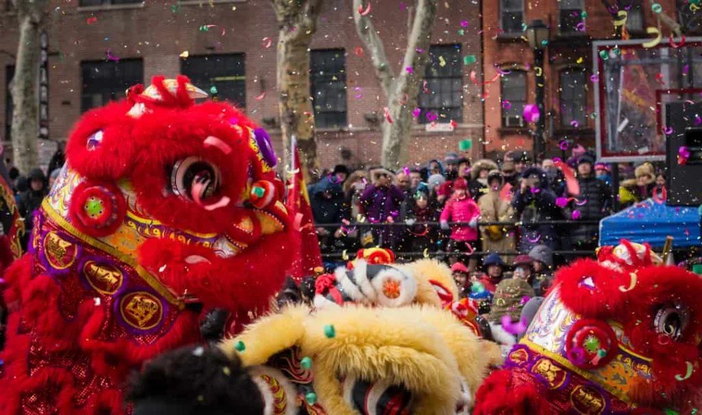 Kleurrijke lionsdance kostuums met rode en gouden koppen tijdens een optocht voor Chinees Nieuwjaar in Chinatown New York, met confetti in de lucht en toeschouwers op de achtergrond