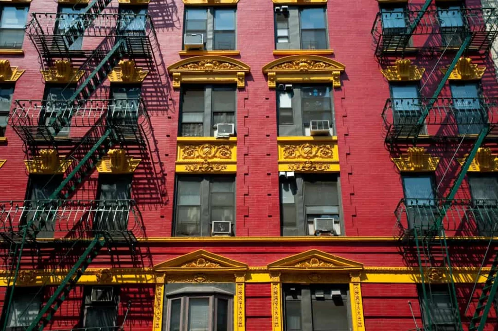 Rode bakstenen gevel met gouden sierlijsten en zwarte brandtrappen aan een woongebouw in Chinatown New York