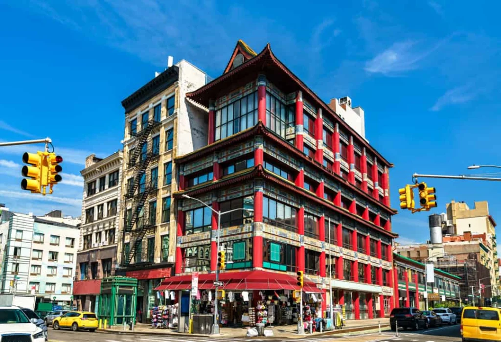 Opvallend rood gebouw met pagodedaken en gouden details op een straathoek in Chinatown New York, met verkeerslichten en gele taxi's ervoor