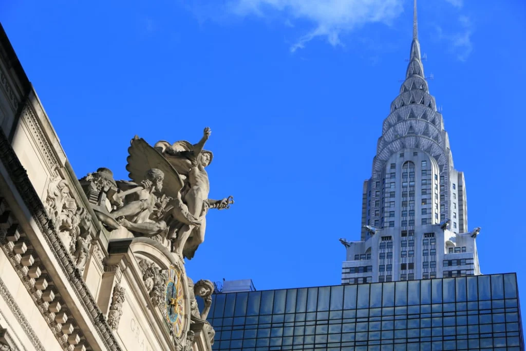 Gouden top van de Chrysler Building tegen een blauwe lucht met op de voorgrond het beeldhouwwerk van Grand Central Terminal