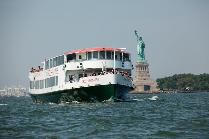 Een groene en witte veerboot van Circle Line vaart langs het Vrijheidsbeeld met passagiers aan dek