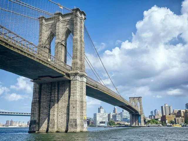 Onderaanzicht van de stenen pijler en kabels van de Brooklyn Bridge met de skyline van New York City op de achtergrond