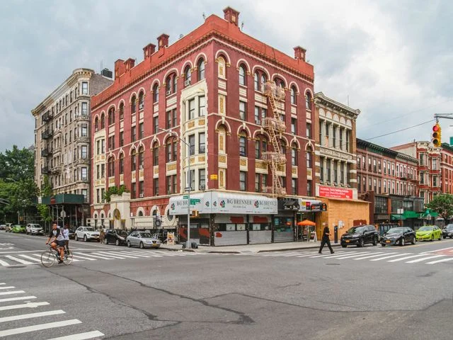Straathoek in New York City met een opvallend rood bakstenen hoekgebouw, geparkeerde auto's en een fietser die oversteekt