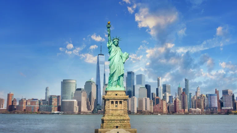 Het Vrijheidsbeeld op zijn sokkel met daarachter de skyline van Manhattan onder een blauwe lucht met wolken