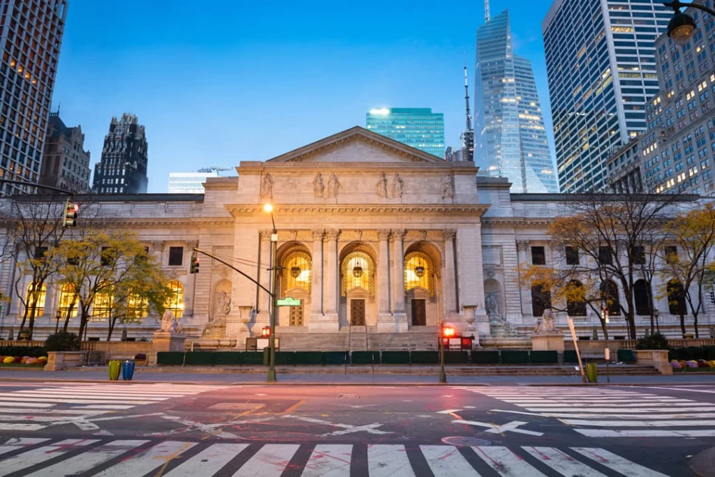 De New York Public Library met verlichte ramen bij schemering, omringd door wolkenkrabbers op een lege kruising