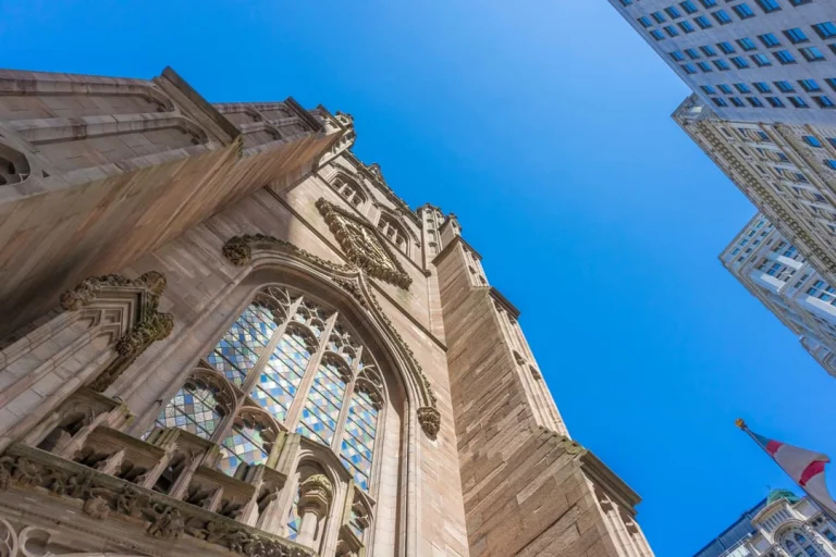 Close-up van de versierde gotische gevel en spits van Trinity Church tegen een strakblauwe lucht met wolkenkrabbers op de achtergrond