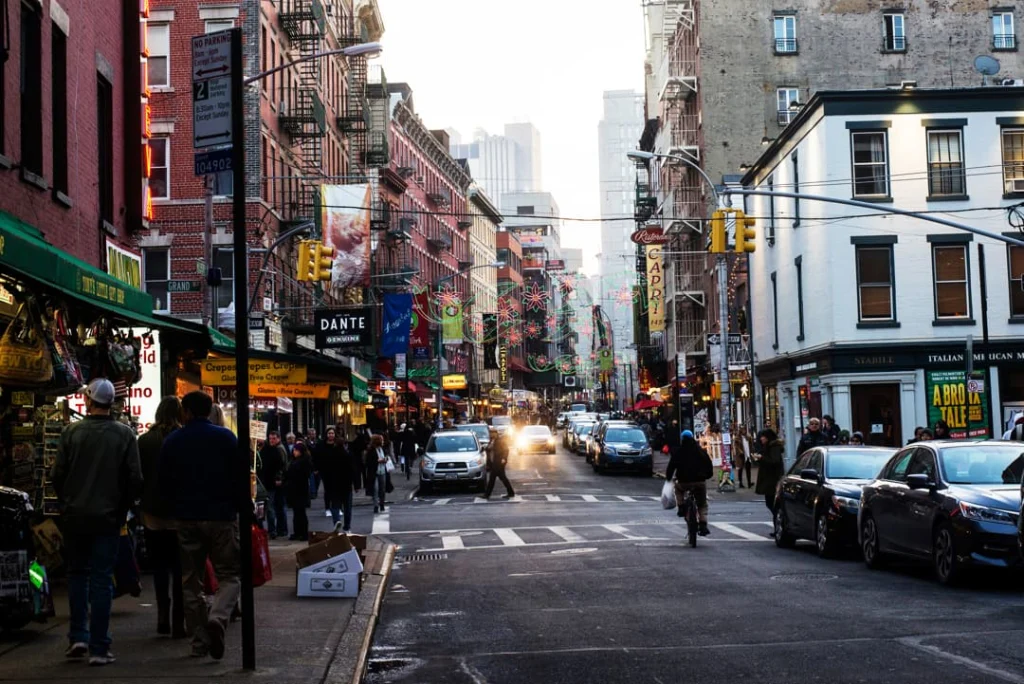 Voetgangers en verkeer op een levendige straat in Little Italy in New York met winkels, kraampjes en kleurrijke versieringen