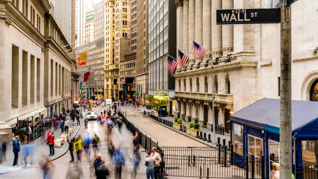 Wazig gefotografeerde voetgangers en verkeer op Wall Street met de zuilengevel van de effectenbeurs en wapperende vlaggen