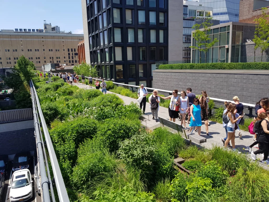 Een groep bezoekers loopt over het verhoogde wandelpad van de High Line, omringd door weelderige beplanting en moderne glazen gebouwen in New York