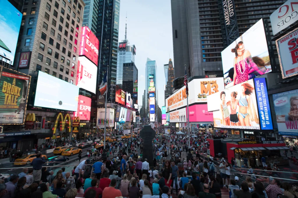 Grote menigte mensen op Times Square tussen fel verlichte billboards en gele taxi's in de avond