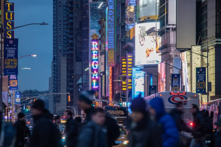 Wazige menigte voetgangers loopt over straat tussen felgekleurde neonreclames en bioscoopborden op Times Square in de schemering