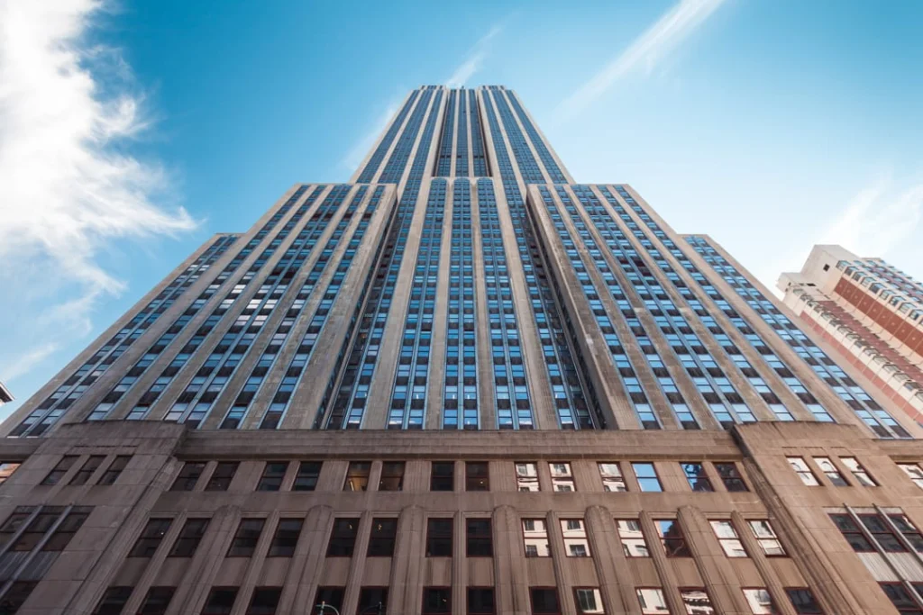 Blik recht omhoog naar de gevel en top van het Empire State Building met wolkenpartijen tegen een felblauwe hemel