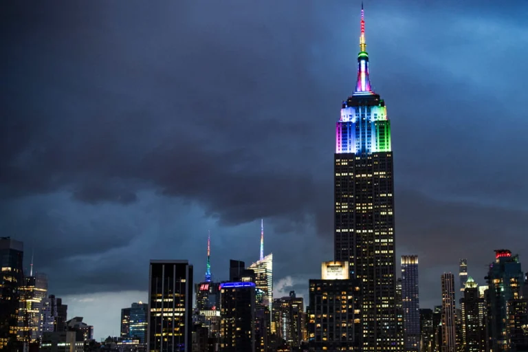Empire State Building die 's nachts oplicht in felle regenboogkleuren boven de donkere skyline van Manhattan tijdens Pride