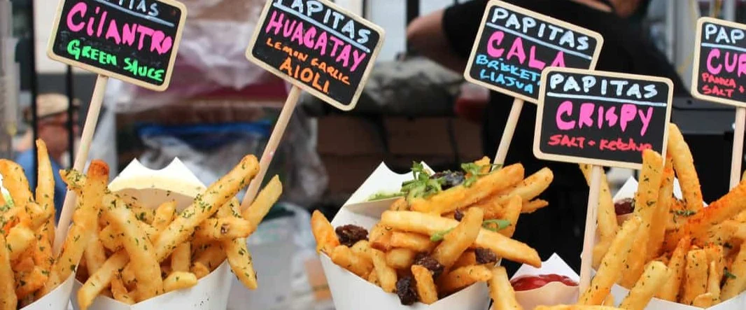Bekertjes friet met verschillende smaken staan uitgestald voor handgeschreven bordjes met de namen van de sauzen op een streetfoodmarkt