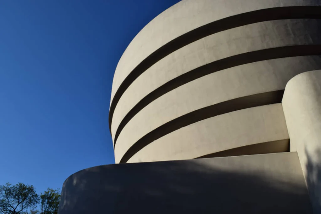 Detailopname van de spiraalvormige betonnen gevel van het Guggenheim Museum met horizontale lijnen tegen een blauwe lucht