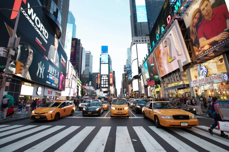 Rij gele taxi's en auto's stopt voor een zebrapad op Times Square, omringd door hoge gebouwen vol reclameborden
