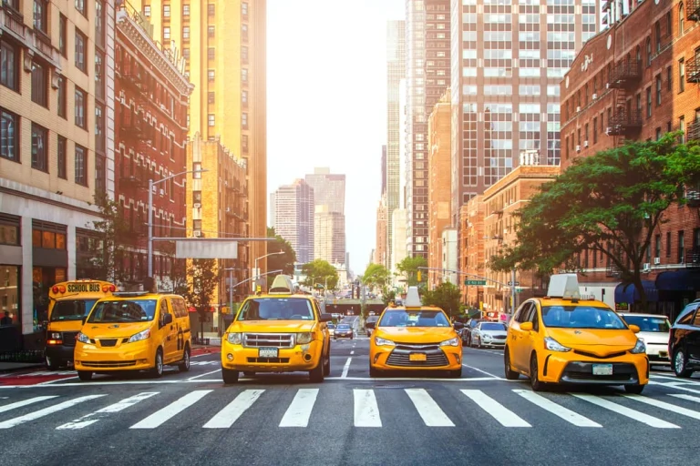 Rij gele taxi's en een schoolbus stoppen bij een oversteekplaats tussen hoge gebouwen in Manhattan, New York