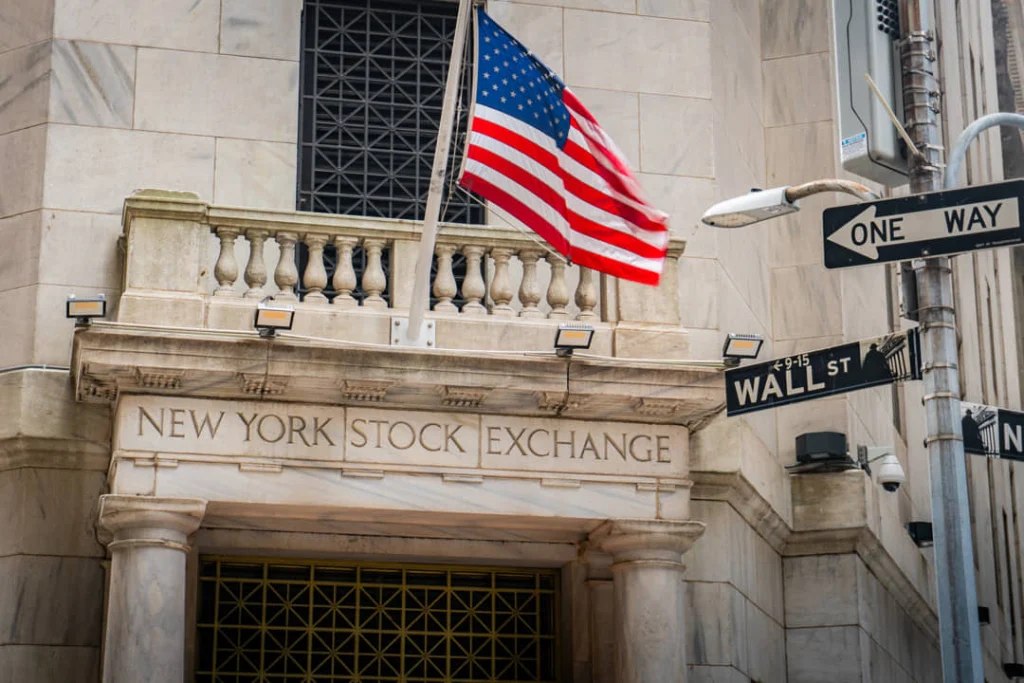 Klassieke zuilengevel van de New York Stock Exchange met een Amerikaanse vlag en het straatbord van Wall Street ernaast