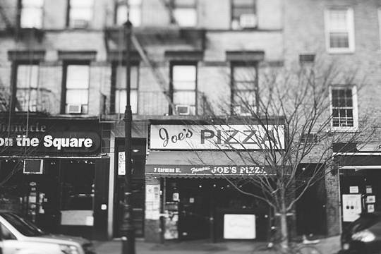 Zwart wit foto van de gevel van pizzeria Joe's Pizza met brandtrappen aan het gebouw erboven in Greenwich Village