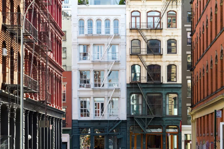 Rij smalle historische gebouwen met sierlijke gevels en zwarte brandtrappen naast elkaar in een straat in Greenwich Village