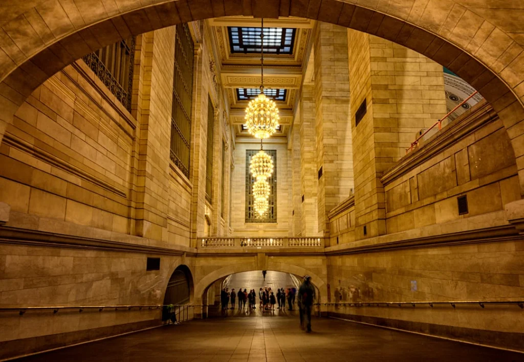 Warm verlichte gewelfde doorgang in Grand Central Terminal met sierlijke kroonluchters en een groep reizigers die de gang doorlopen