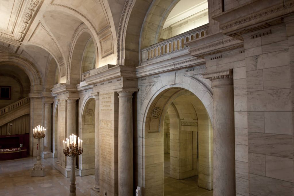 Stenen gewelfde gang met bogen, marmeren zuilen en twee grote kandelaars in de New York Public Library