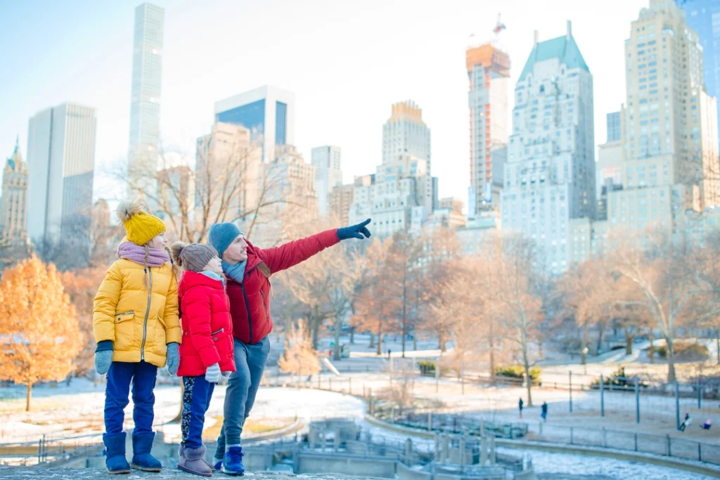 Vader met twee kinderen in winterjassen wijst naar de wolkenkrabbers rond Central Park in New York tijdens de winter