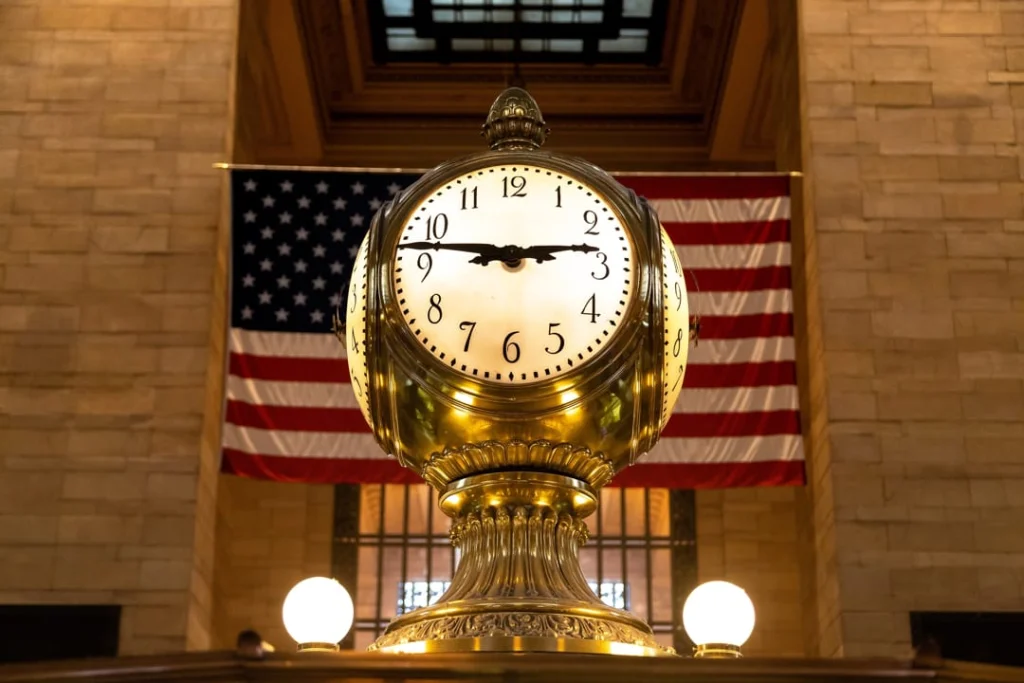 Detailopname van de bekende gouden vierzijdige klok in Grand Central Terminal met een grote Amerikaanse vlag op de achtergrond