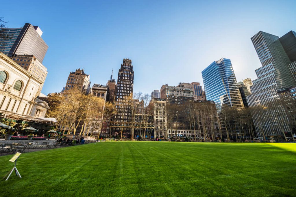 Zonovergoten grasveld van Bryant Park met daaromheen historische en moderne gebouwen tegen een strakblauwe lucht