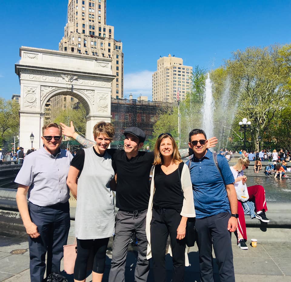 Vijf lachende reizigers poseren voor de boog en fontein van Washington Square Park op een zonnige dag in New York