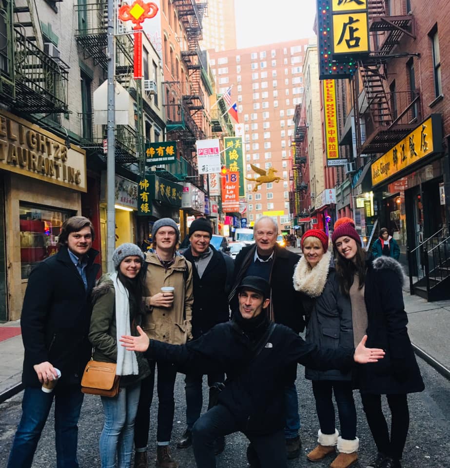 Acht reizigers staan gebroederlijk bijeen in een smalle straat vol Chinese neonreclames en winkels in Chinatown New York