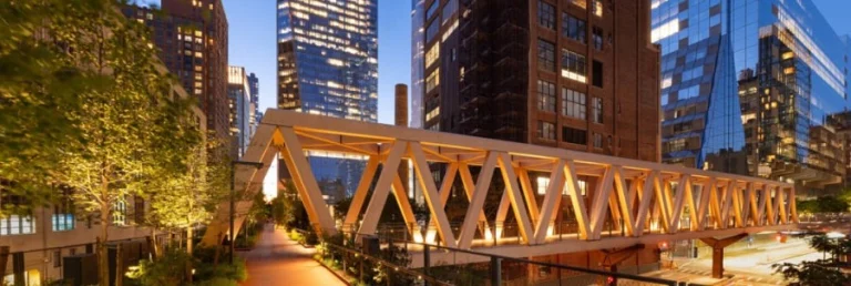 Verlichte houten brugconstructie van het High Line park in New York met wolkenkrabbers op de achtergrond bij avondschemering