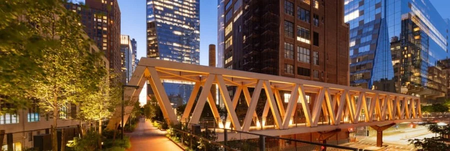 Verlichte houten brugconstructie van het High Line park in New York met wolkenkrabbers op de achtergrond bij avondschemering