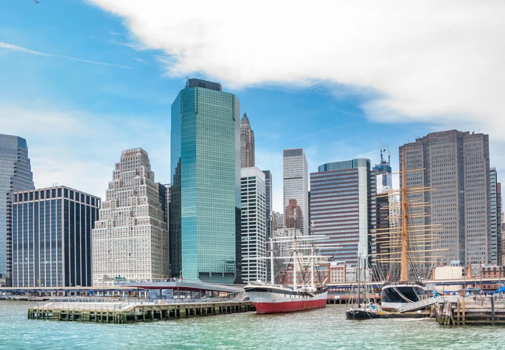 Oude zeilschepen liggen afgemeerd aan de pier met de wolkenkrabbers van Lower Manhattan op de achtergrond onder een blauwe lucht