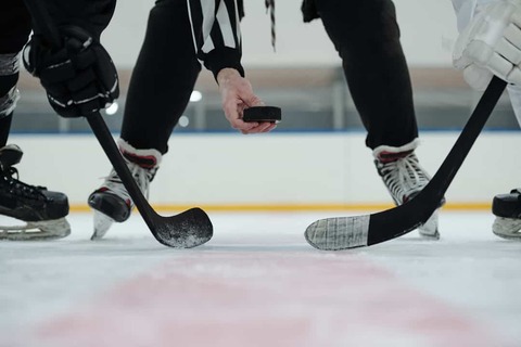 Twee ijshockeyspelers buigen voorover op het ijs terwijl de scheidsrechter de puck laat vallen voor de faceoff