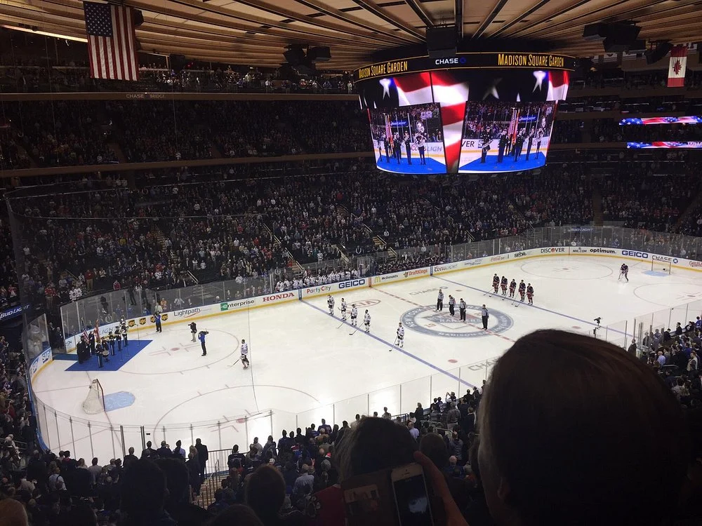 Volle tribune kijkt naar spelers op het ijs tijdens een wedstrijd in Madison Square Garden met Amerikaanse en Canadese vlaggen