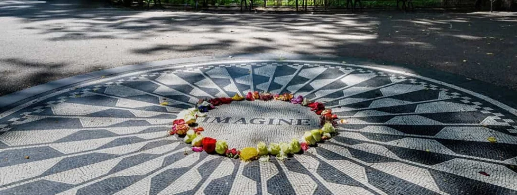 Zwart wit mozaïek met het woord Imagine in het midden, omringd door verse bloemen als eerbetoon in Strawberry Fields