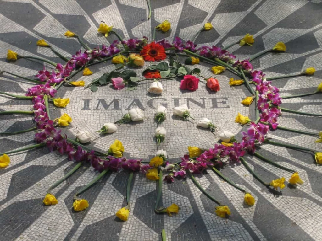 Zwart wit mozaïek met het woord Imagine, omringd door paarse, witte en gele bloemen in de vorm van een vredesteken