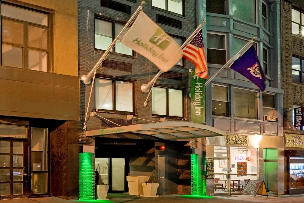 Verlichte ingang van een Holiday Inn hotel in New York in de avond, met vlaggen boven de deur