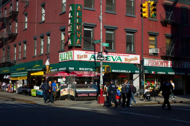 Gevel van de kaaswinkel Alleva met rode bakstenen muur en groene luifels in Little Italy in New York, met voetgangers op straat